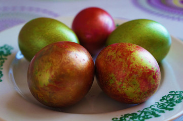 Green and red easter eggs on a white plate with ornament.