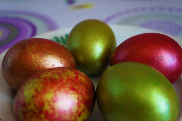 Green and red easter eggs, close-up on a white plate with ornament. On the table with circles. 