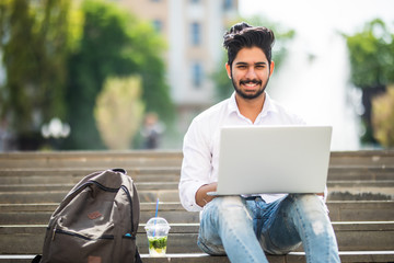 Handsome young indian man working on laptop while sitting outdoors on the stairs, concept of work...