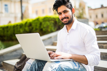 Handsome young indian man working on laptop while sitting outdoors on the stairs, concept of work...