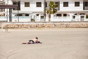 Fat man sunbathing on beach in black swimwear on empty beach