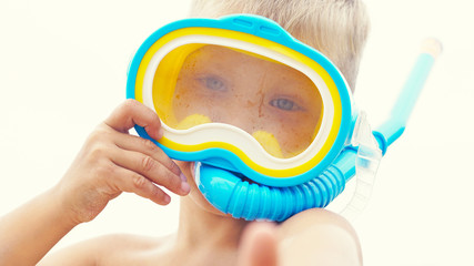 Little Caucasian boy playing with snorkeling equipment standing on sand on tropical beach.