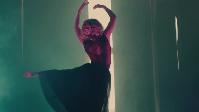 a young woman performs active graceful movements to music on the stage of a small theater, a lady jumps up with her hands up, she is dressed in a gorgeous dress