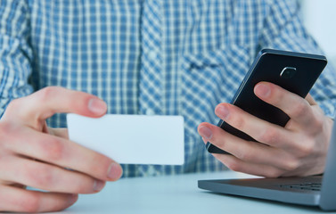 Middle section of young businessman talking on the phone and holding business card at workplace.