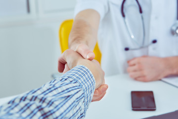 Close up of a male doctor shaking hands with his male patient. Medicine and trust concept
