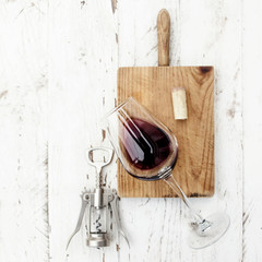  A glass of red wine, bottle, corkscrew  and wine corks on rustic board over  white wooden table,...