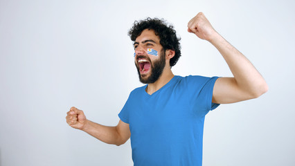 Sport fan screaming for the triumph of his team. Man with the flag of Uruguay makeup on his face...