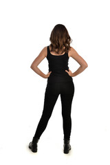 Fototapeta premium full length portrait of brunette girl wearing black singlet, jeans jeans and boots. standing pose, with back view. isolated on white studio background.