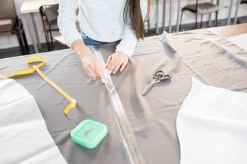 High angle close up of unrecognizable female tailor tracing fabric with white chalk while sewing...