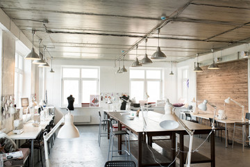 Wide angle shot of modern atelier interior with wooden workstation in foreground and sewing...