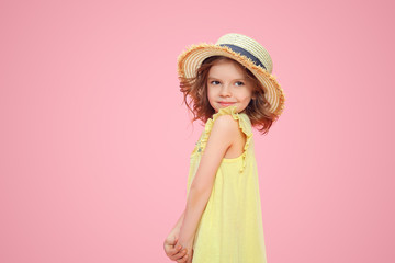 Obraz na płótnie Canvas Close up portrait of a Beautiful girl in yellow dress and straw hat. Pretty tenderness kid looking away, posing on a pink studio background.