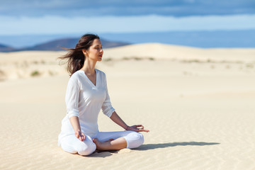 Fototapeta na wymiar Young woman meditating in Lotus Pose in desert on Canary Islands, Spain.
