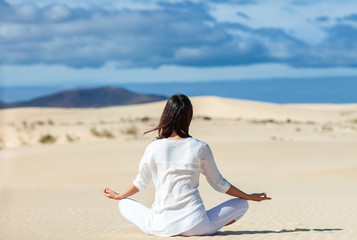 Fototapeta na wymiar Back view of young woman meditating in Lotus Pose in desert