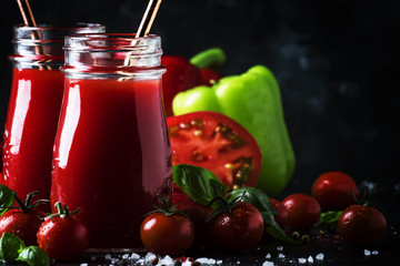 Healthy and useful spicy smoothies or juice from red tomatoes and bell peppers with green basil in glass bottles on a dark background, selective focus