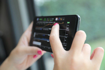 Female hand with smartphone trading stock online in coffee shop , Business concept