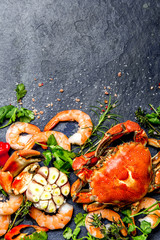 Fresh raw seafood - shrimps and crabs with herbs and spices on dark gray background. Copy space. Vertical