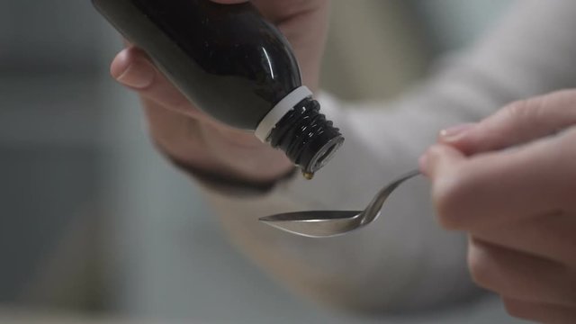 Woman pouring cough syrup into spoon, flu epidemic, herbal remedies, closeup