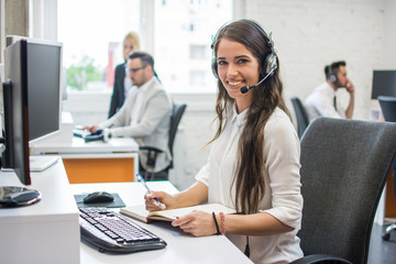 Portrait of beautiful and cheerful young woman telephone operator agent with headset working in...