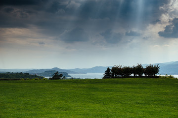 Fototapeta na wymiar panorama of Lake Maggiore green woods around and cloudy sky with rays of light, storm approaching