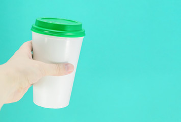 white plastic coffee cup with green lid in hand on a blue background, front view with copy space