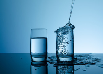 Creative splashing water in the glass on blue background.