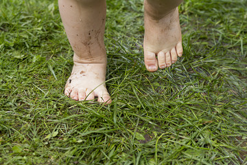 Dirty legs of child in summer on grass without shoes close-up