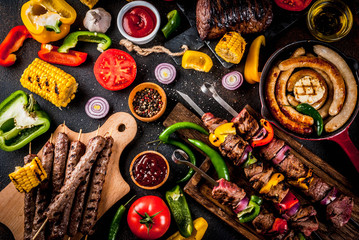 Assortment various barbecue food grill meat, bbq party fest - shish kebab, sausages, grilled meat fillet, fresh vegetables, sauces, spices, dark rusty concrete table, above copy space - obrazy, fototapety, plakaty