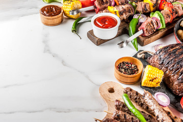 Assortment various barbecue food grill meat, bbq party fest - shish kebab, sausages, grilled meat fillet, fresh vegetables, sauces, spices, white marble background, above copy space