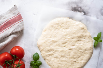 Dough for pizza or focaccia with ingredients, tomatoes, basil, olive oil. Top view.