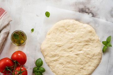 Dough for pizza or focaccia with ingredients, tomatoes, basil, olive oil. Top view.