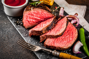 Fresh grilled beef, homemade bbq meat medium rare, on black stone cutting board, with spices, dark background, copy space