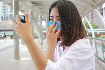 Skin care concept, Beautiful asian girl using oil remover paper on her face and looking at smartphone on street background
