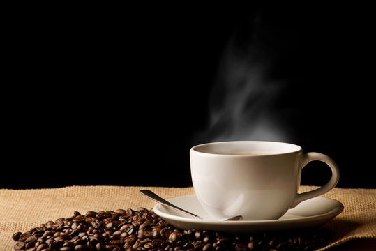 Cup of coffee with smoke and coffee beans on wooden background © Pcess609