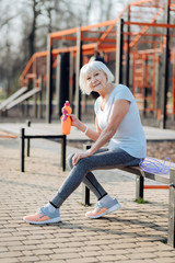 My rest. Happy slim woman holding a bottle of juice and relaxing while exercising
