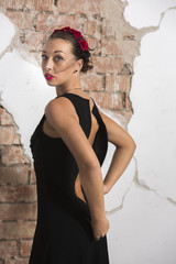Sexy young girl in a long black dress with heels, with red lips and an attractive smile floral rim in her hair poses in the loft studio intimately taking off the dress