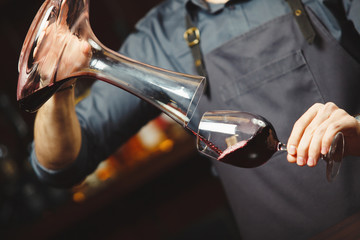 Sommelier pouring wine into glass from mixing bowl. Male waiter