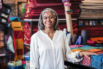 Fototapeta na wymiar Smiling mature woman standing by cloth in her fabric store