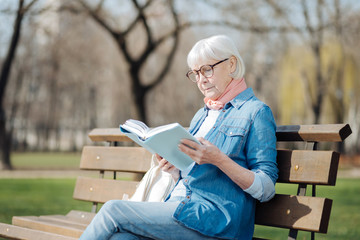 Avid reader. Involved blond woman reading a book while sitting on the bench