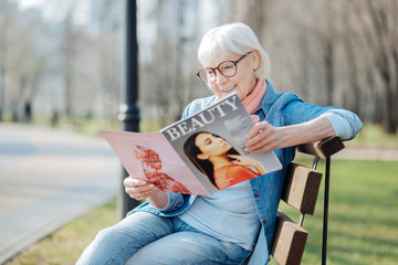New trends. Smiling blond woman reading a magazine while sitting on the bench