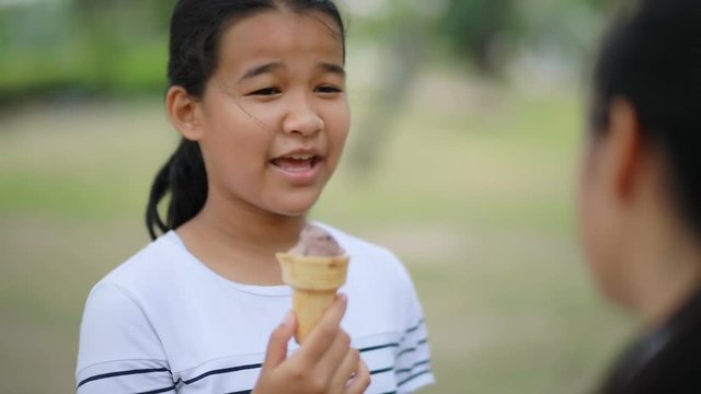 asian teenager eating icecream and talking to friend in public park