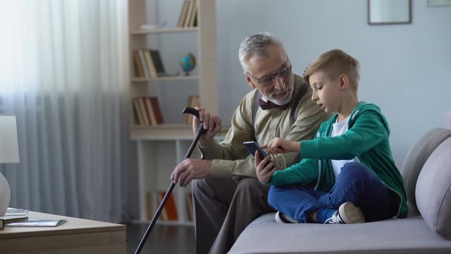 Boy explaining to grandpa how to use cell phone, simple technologies for old man