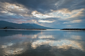 Cloud reflections in a water of aegean sea at sunrise, Volos harbor with Pelion mountain in background, Greece