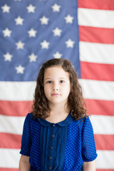 Little girl standing in front of an American flag background