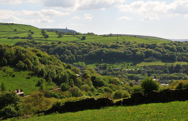 springtime pennine countryside in calderdale west yorkshire with typical hillside fields, woodland, houses and stoodley pike monument in the distance