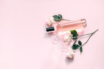 White roses, wine and glasses for wine on a soft light pink on wood table. Flat lay, top view, copy space 
