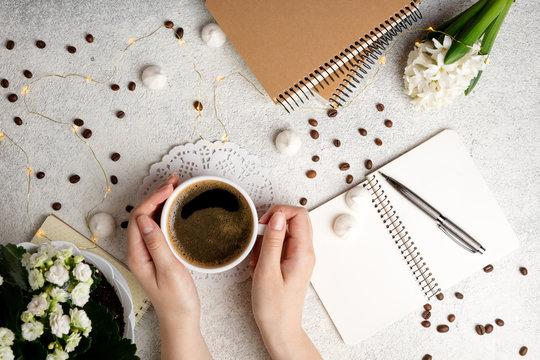 Flat lay feminine background with coffee cup, notebooks and flower hyacinth. Female hands holding coffee cup. Cozy weekend at home concept. Top view