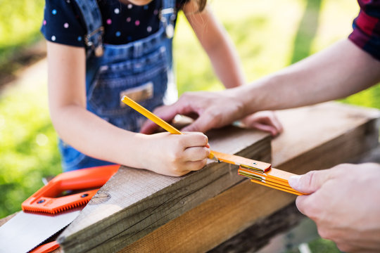 Father with a small daughter outside, making wooden birdhouse.