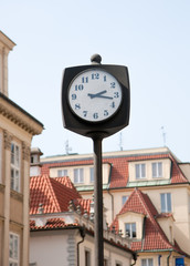 Fototapeta na wymiar Street clock. In the background of the house with tiled roofs