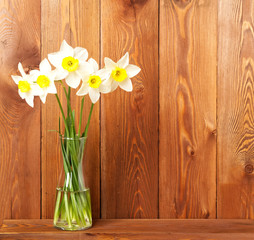 Bouquet of fresh flowers, daffodils in vase on wooden table, opposite brown wooden wall. Empty space for text.