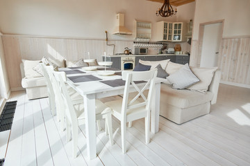 Wide angle shot of modern dining room with white wooden table and chairs in minimalistic Scandinavian design lit by sunlight, copy space, nobody